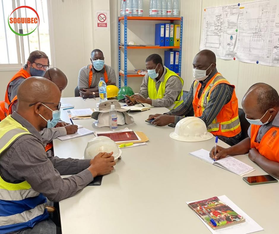 Réunion de chantier de la SOGUIBEC : les équipes en gilets de sécurité autour d'une table, plans affichés au mur