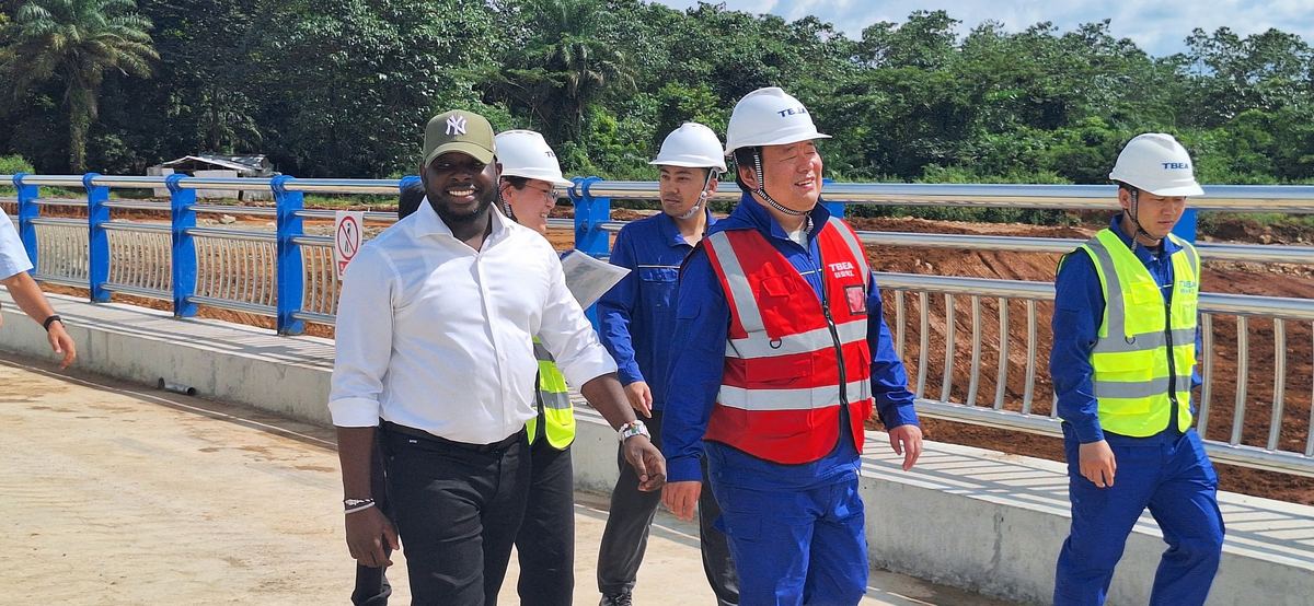 Traversée à pied d'un pont achevé aux garde-corps bleus : le Président-Directeur Général souriant, entouré des partenaires techniques